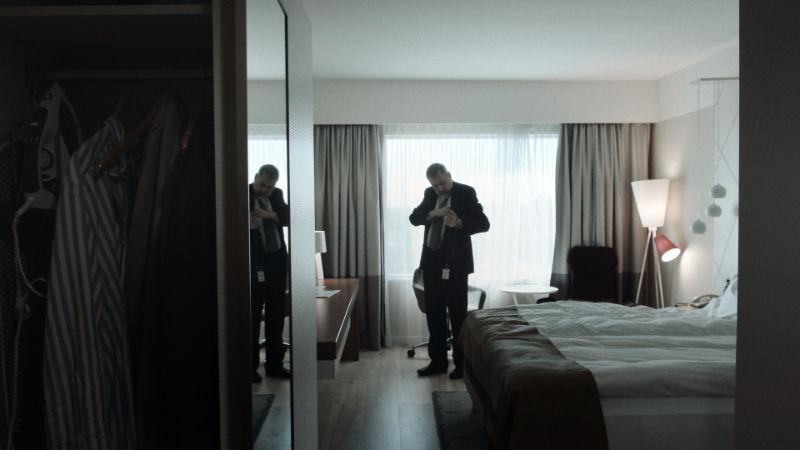 Filmstill aus "This Kind of Hope": In einem nüchternen Hotelzimmer steht ein Mann vor dem Bett und steckt etwas in die Innenseite seines Jacketts.