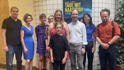 Eine Gruppe von neun Menschen, festlich gekleidet, vor dem Kinoplakat von "Tage mit Naadirah".