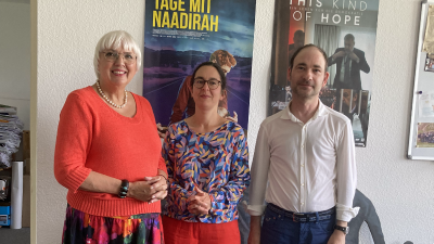 Zwei Frauen (Claudia Roth und Claudia Macher) und Ein Mann (Thomas Kral) stehen in einem Büro vor zwei Filmplakaten von "Tage mit Naadirah" und "This Kind of Hope".