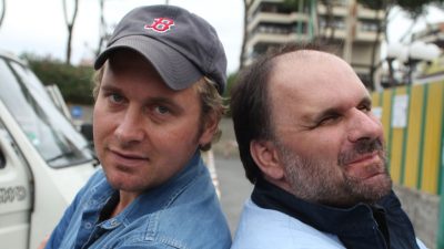 Zwei Männer stehen Rücken an Rücken vor einem VW-Bully.