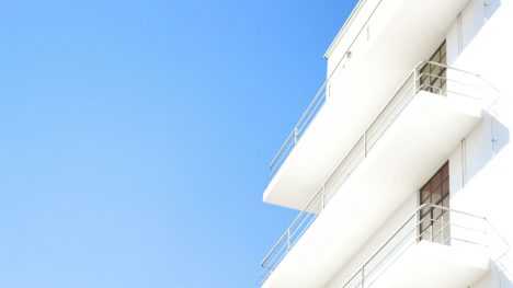 Perfekter blauer Himmel, am rechten Rand ein weißes mehrstöckiges Gebäude mit Außenbalkonen.