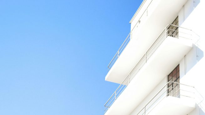 Perfekter blauer Himmel, am rechten Rand ein weißes mehrstöckiges Gebäude mit Außenbalkonen.